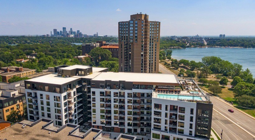 A tall building with a pool on the roof is in the foreground with a city skyline in the background.