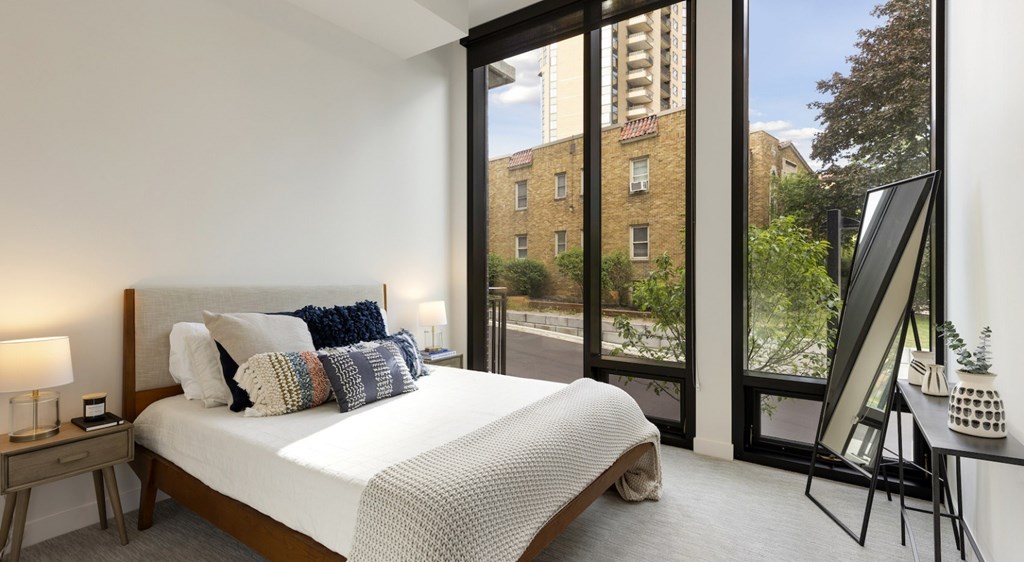 A bedroom with a large bed and a view of a building outside the window.