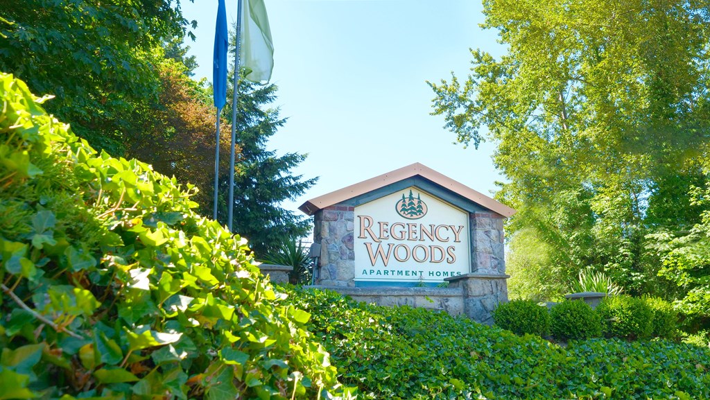 A sign for Regency Woods Apartment Homes is surrounded by greenery.