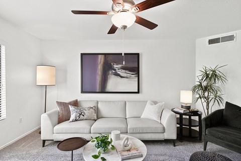 A living room with a white couch, a ceiling fan, and a painting on the wall.
