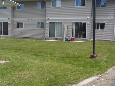 A grassy area in front of a grey building with a red post in the foreground.