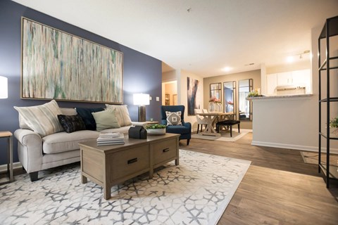 A modern living room with a white sofa, a wooden coffee table, and a large abstract painting on the wall.