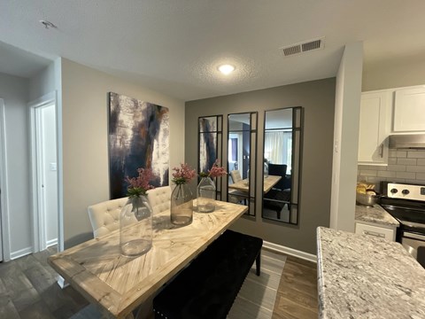A dining table with a vase on it and a kitchen area in the background.