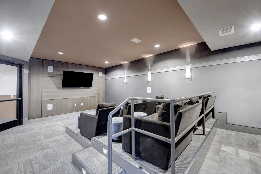A cozy home theater here at Sorrel Fairview Apartment Homes with tiered seating features plush gray couches facing a wall-mounted TV. Soft lighting and modern decor create an inviting atmosphere.