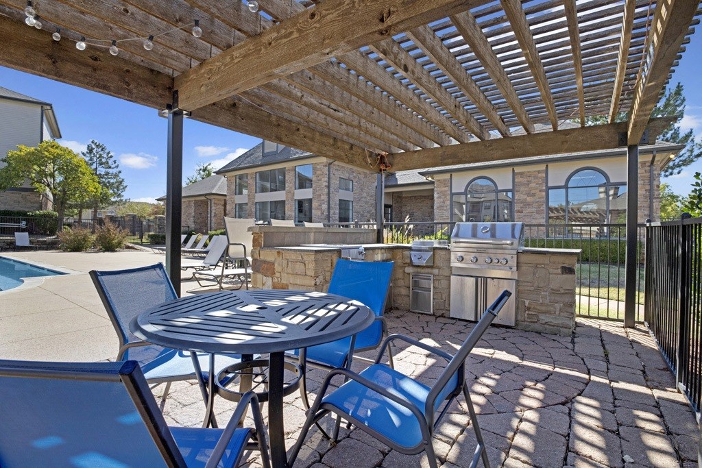 a patio with a pergola and a barbecue grill next to a pool