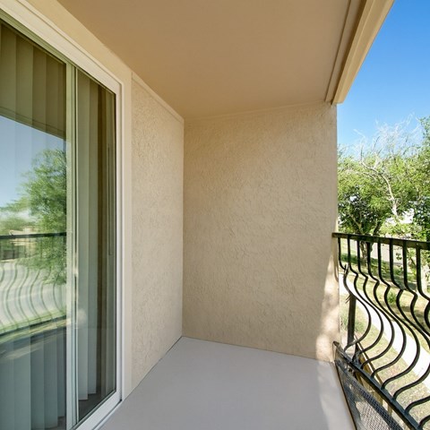 A private outdoor balcony here at Avalon Springs with a covered ceiling, textured neutral walls, and a sliding glass door, featuring a black metal railing and peaceful views of surrounding greenery for a quiet, relaxing outdoor retreat.