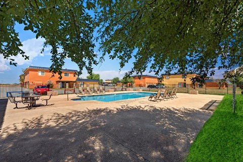 A pool surrounded by chairs and a fence with trees in the background.