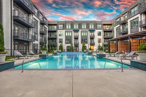 A beautiful pool courtyard here at Crosby at the Brickyard with a sparkling pool, modern buildings, private balconies, lounge seating, and a colorful sunset sky, creating a relaxing, upscale outdoor retreat.