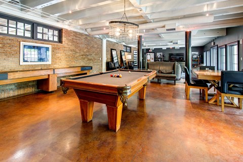 A pool table is in the middle of a room with a brick wall.