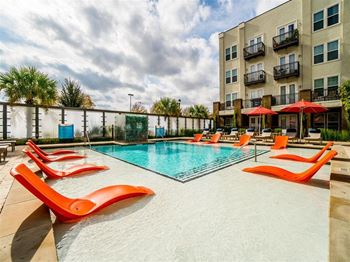 a swimming pool with orange chairs and umbrellas in front of an apartment building