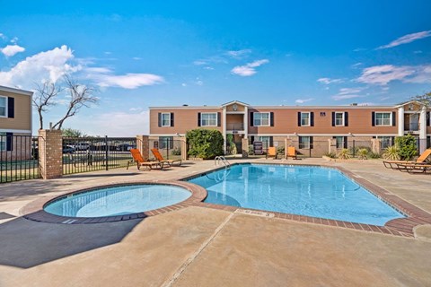 A refreshing outdoor swimming pool here at Golden Crest with clear blue water, a spacious concrete deck, and surrounding lounge chairs, featuring a separate shallow pool area and a fenced courtyard setting under bright, sunny skies.