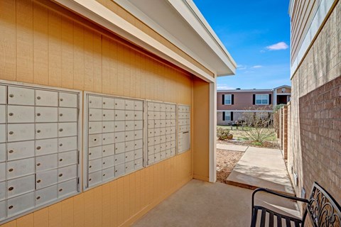A covered community mailbox area here at Golden Crest with neatly organized mailboxes, neutral-toned siding, and a shaded walkway that leads into the landscaped courtyard, offering a convenient and accessible mail pickup space.