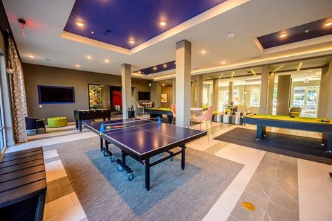A modern game room here at Harmony Luxury featuring a ping pong table, pool tables, lounge seating, and mounted TVs, enhanced by stylish lighting, open layout, and a lively, social atmosphere for residents to enjoy.