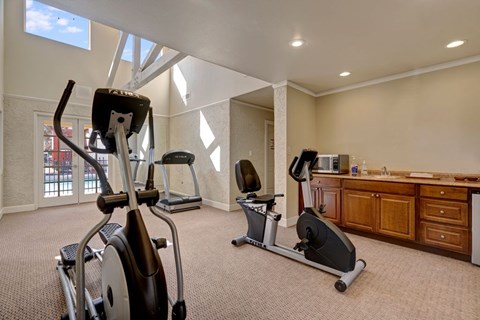 A well-equipped fitness center here at Las Colinas with cardio machines, including treadmills and stationary bikes, set on plush carpeting. Large windows and bright lighting create an open, energizing space, with a convenient counter area adding comfort for residents during workouts.