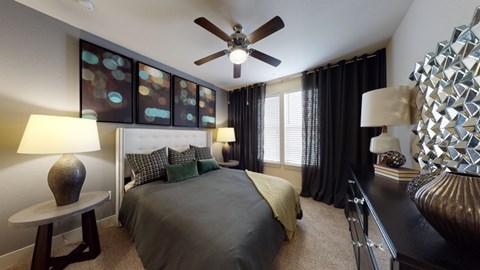 A bedroom with a bed, a ceiling fan, and a side table with a lamp.