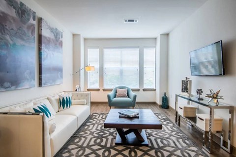 A living room with a white couch, a blue chair, and a painting on the wall.