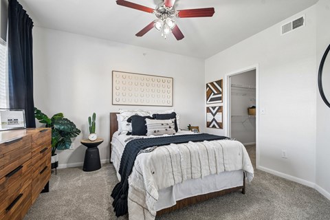 A bedroom with a bed, a dresser, a ceiling fan, and a wall hanging.