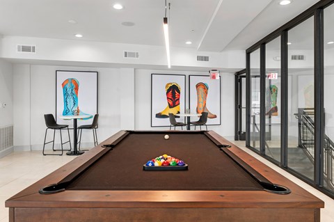 A game lounge here at Reserve at Arboretum with a dark wood pool table and brown felt, bright modern lighting, colorful boot artwork, and small café tables, creating a clean, social, and welcoming hangout space.
