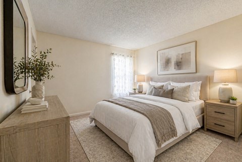 A bedroom with a large bed, a nightstand, and a plant on a dresser.