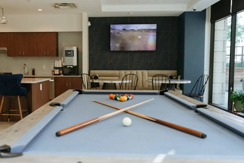 A stylish resident lounge here at Valor at the Realm with a pool table, modern seating booths, café-style tables, a coffee station, and a wall-mounted TV, featuring large windows and a social, upscale atmosphere.