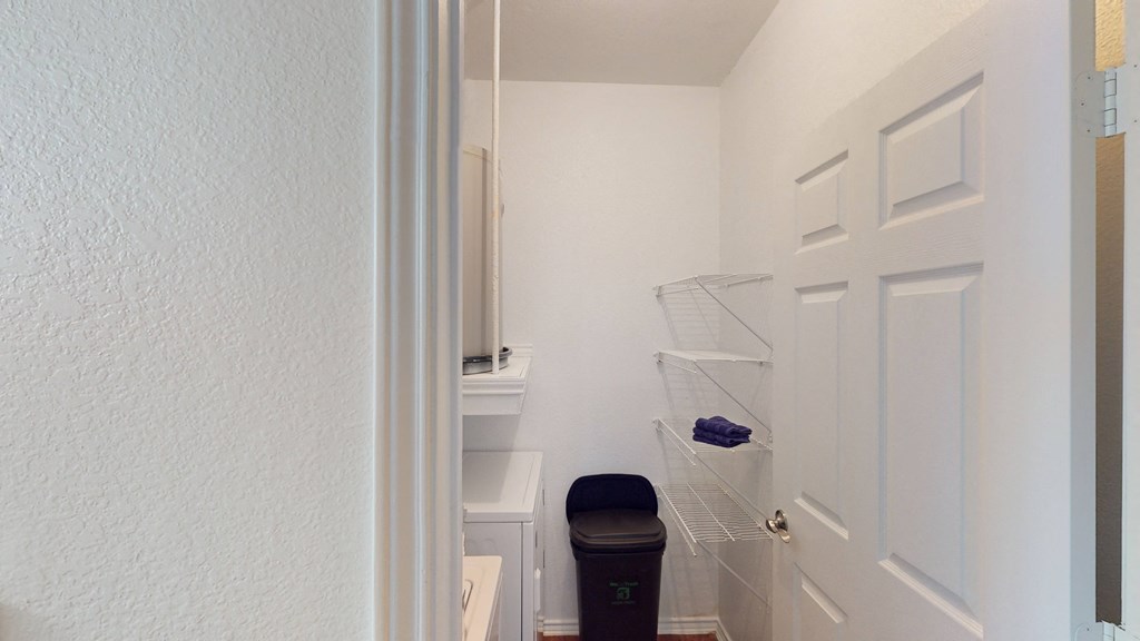 a small closet in a bathroom with a trash can and a white door