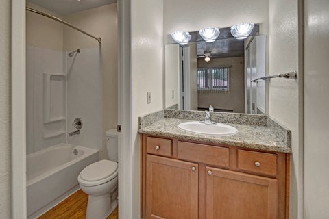 Compact bathroom here at The Club at Eagle Pointe Apartments with wooden vanity, granite countertop, and a white sink. A large mirror reflects a bright room with a window and ceiling fan.
