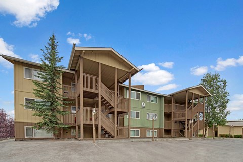 The Club at Eagle Pointe Apartments building with wooden exterior, green and beige tones. Three-story structure with staircases, surrounded by trees under a clear blue sky.