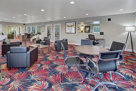 Modern office lobby here at The Club at Eagle Pointe Apartments with vibrant red and blue floral carpet, featuring gray armchairs, wood tables with orchids, and sleek black office chairs. Bright and welcoming atmosphere.