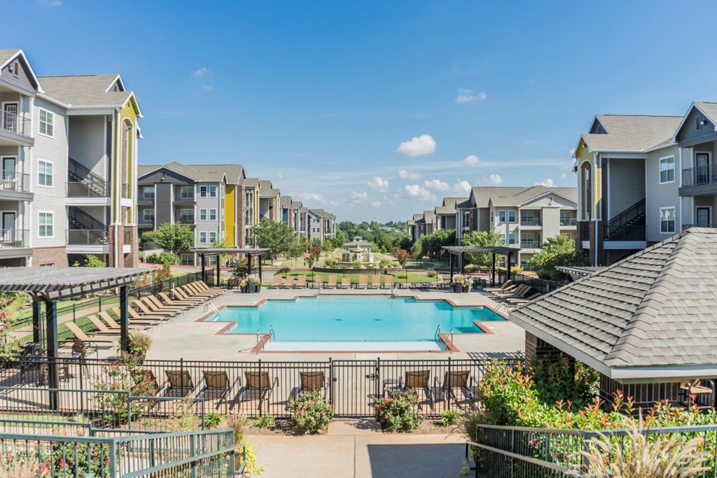 Lincoln at Central Park Apartment Homes with modern, three-story buildings surrounding a clear blue swimming pool. Sun loungers and shaded areas create a relaxed atmosphere.