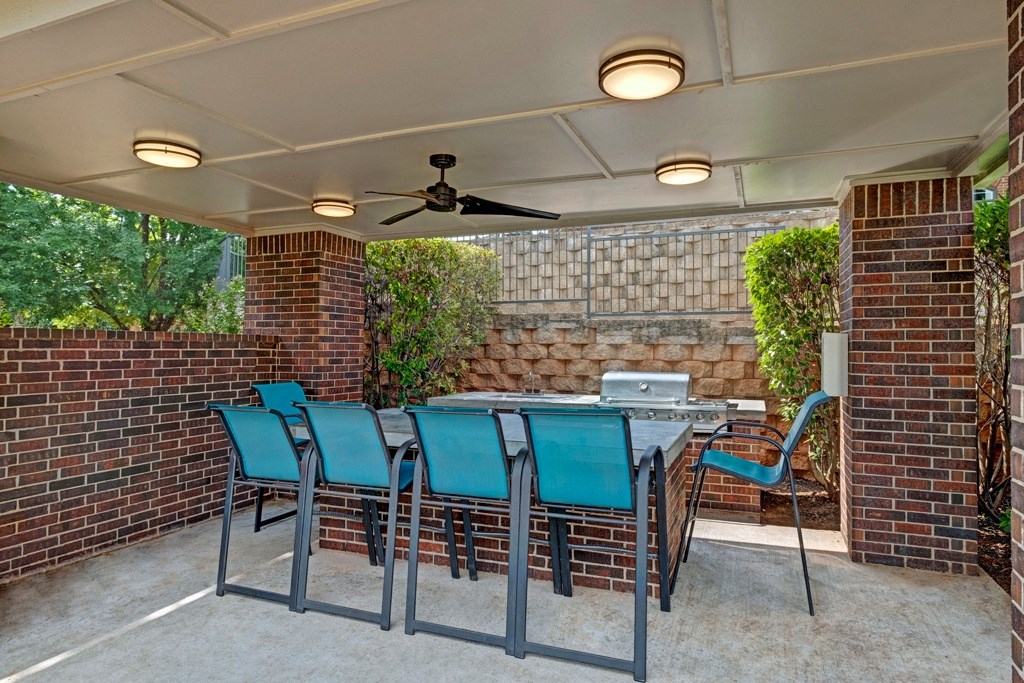 Covered patio here at Lincoln at Central Park Apartment Homes with a ceiling fan and brick columns surrounds an outdoor dining area. Blue chairs and a grill create a relaxed, inviting atmosphere.