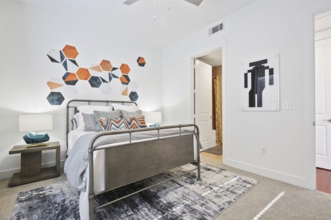A modern bedroom here at The Uptown Apartment Homes with a metal bed frame, geometric wall art, robot poster, and stylish gray rug. Bright, minimalist, and playful atmosphere.