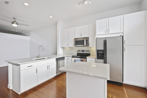 Modern kitchen here at The Uptown Apartment Homes with white cabinets, stainless steel appliances, and a central island with a white countertop. Bright and spacious with hardwood floors.