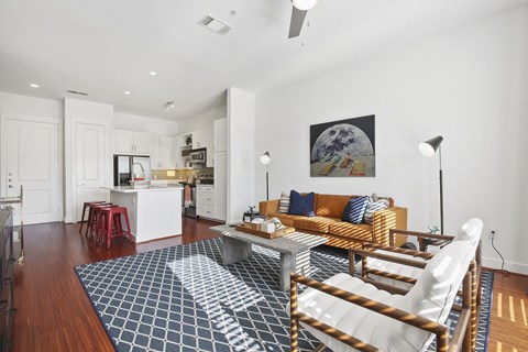 A modern living room here at The Uptown Apartment Homes with a white wall and hardwood floor features a brown leather sofa, blue patterned rug, and minimalist decor, creating a cozy atmosphere.