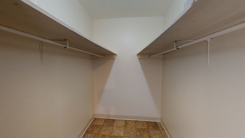 Empty walk-in closet here at the Village at Calais Apartments with beige walls, two white shelves on opposite sides, and tiled floor. The space appears clean, spacious, and well-lit.