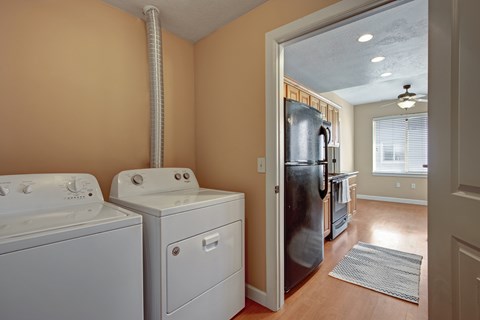 A laundry room with a washer and dryer and a refrigerator in the background.