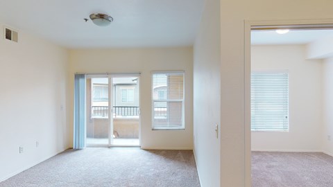 A spacious room with a carpeted floor and a sliding glass door leading to a balcony.