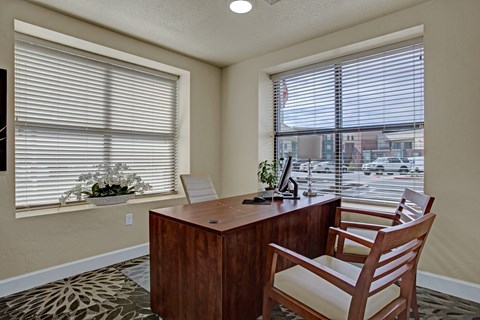A room with a desk and a chair in front of a window with blinds.