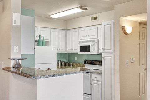 A kitchen with white cabinets and a granite counter.