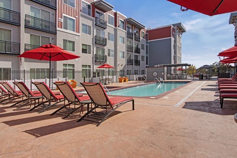 A pool area with red umbrellas and chairs.