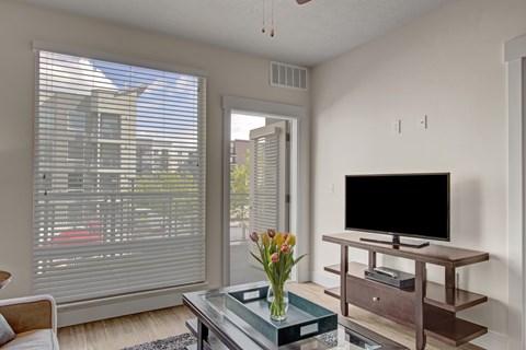 A living room with a television and a vase of flowers on a coffee table.
