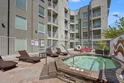 A pool surrounded by chairs and a fence in front of apartment buildings.