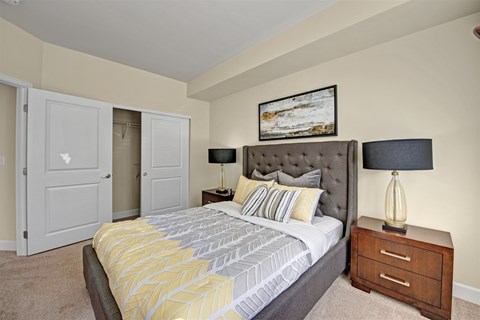 A bedroom with a large bed, a nightstand with a lamp, and a painting on the wall.
