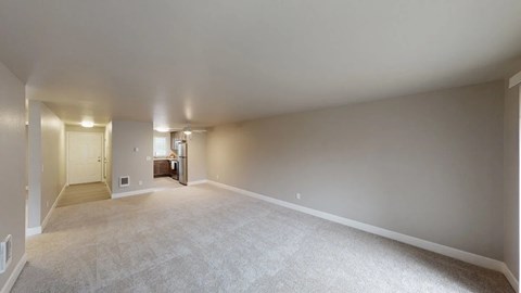 A living and dining area here at A'Cappella with soft gray walls, wide open carpeted floor, bright entry hall, and open view toward the kitchen, creating a spacious, clean, and welcoming empty layout.