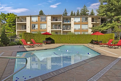 A swimming pool with red chairs and umbrellas in front of a building.