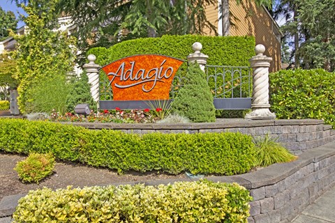 A sign that says Adagio in front of a hedge.