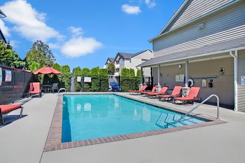 A swimming pool with red lounge chairs and a metal fence.