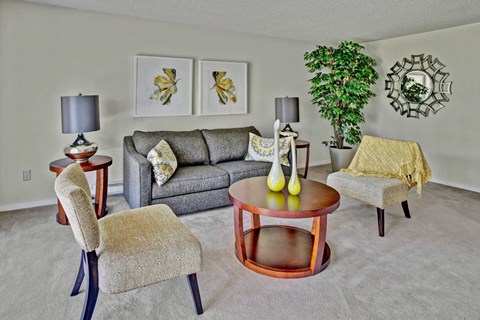 A living room with a grey couch, a round table, and a chair with a wooden frame.