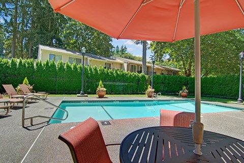 A patio with a table, chairs and an umbrella overlooking a pool.