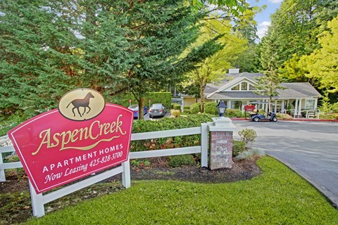 A sign for Aspen Creek Apartment Homes is displayed in front of a house.