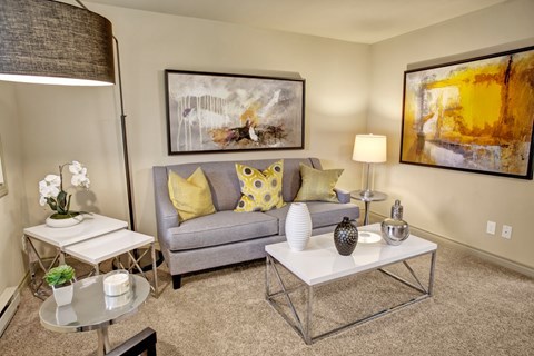 A living room with a grey couch, a white coffee table, and a painting on the wall.